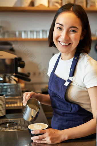 垂直拍摄友好的咖啡师女孩微笑准备咖啡倒牛奶使卡布奇诺咖啡