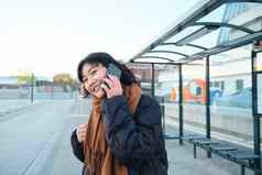 美丽的微笑朝鲜文女孩等待公共汽车停止公共运输会说话的移动电话城市