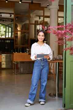 肖像亚洲女人经理站平板电脑前面咖啡馆入口欢迎客人