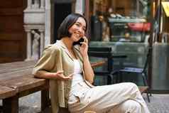 年轻的女人谈话移动电话坐着在户外使电话调用智能手机会说话的