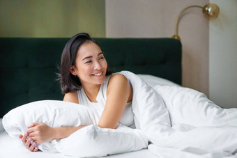 快乐早晨美丽的朝鲜文女人说谎床上微笑醒着的乐观的封面温暖的<strong>羽绒被</strong>