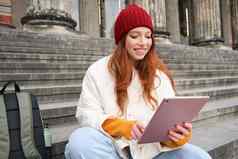 户外拍摄年轻的时尚的红色头发的人女孩坐在楼梯连接公共无线网络数字平板电脑读取新闻小工具