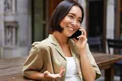 年轻的女人谈话移动电话坐着在户外使电话调用智能手机会说话的
