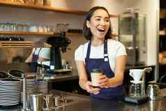 肖像微笑亚洲女孩咖啡师给订单咖啡馆邀请客人选择外卖订单计数器持有外卖杯咖啡