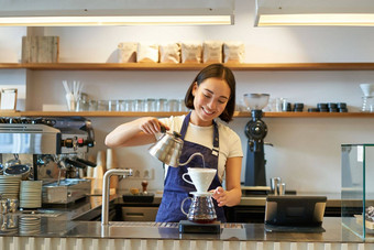 微笑亚洲女孩咖啡师倒热水水壶酝酿过滤器咖啡站计数器咖啡馆
