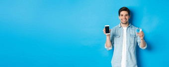 年轻的男人。控制水平衡智能手机应用程序显示移动屏幕应用程序微笑站蓝色的背景
