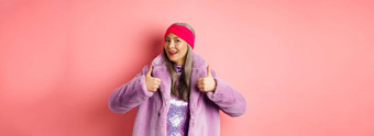 时尚购物概念时尚的亚洲奶奶时尚的高级朝鲜文女人冬天人造革外套显示竖起大拇指批准赞扬好产品粉红色的背景图片