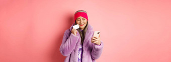 在线购物时尚概念时尚的亚洲祖母使购买互联网智能手机塑料信贷卡粉红色的背景