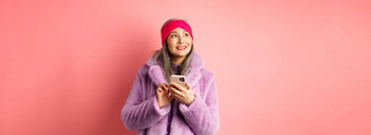 在线购物时尚概念时尚的亚洲高级女人智能手机深思熟虑的脸站粉红色的背景