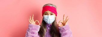 科维德病毒时尚概念特写镜头时尚亚洲高级女人脸面具显示迹象快乐粉红色的背景
