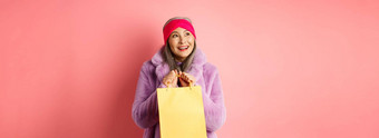 购物时尚概念美丽的亚洲高级女人梦幻上左角落里成像持有黄色的纸袋礼物粉红色的背景