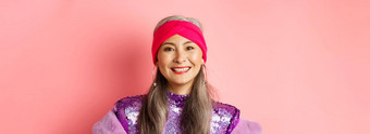 特写镜头时尚的亚洲高级女人灰色头发时尚的迪斯科衣服微笑快乐相机站粉红色的背景