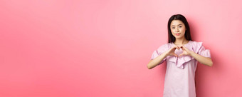 情人节一天概念美女日本青少年女孩显示心手势微笑可爱的表达爱同情情人站浪漫的衣服粉红色的背景