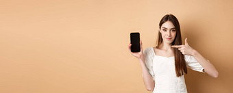 自信女孩指出空智能手机屏幕显示在线促销交易站米色背景