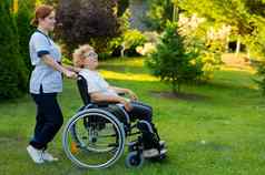 高加索人女医生走上了年纪的病人轮椅公园护士伴随女人走在户外