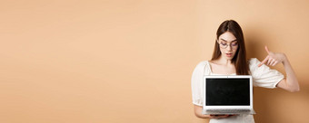 好奇的女孩眼镜指出移动PC屏幕检查在线交易演示项目电脑站米色背景