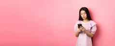 十几岁的亚洲女孩聊天移动电话智能手机屏幕脸站粉红色的背景