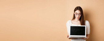 兴奋女孩眼镜显示移动PC屏幕演示在线提供电脑站米色背景