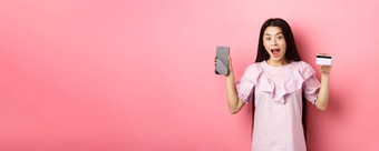 在线购物兴奋亚洲女人显示塑料信贷卡空智能手机屏幕广告互联网商店站粉红色的背景