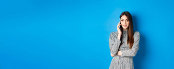 时尚的年轻的女人会说话的电话使<strong>外卖订单</strong>智能手机站衣服蓝色的背景