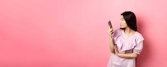 亚洲女孩惊讶智能<strong>手机屏</strong>幕阅读消息站衣服粉红色的背景