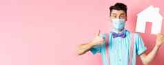 科维德流感大流行真正的房地产概念满意机构客户端显示拇指纸房子断路穿医疗面具站粉红色的背景