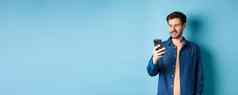 英俊的现代的家伙移动电话阅读智能手机屏幕微笑网络蓝色的背景