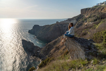女人旅游享受日落海山景观坐在在户外岩石海穿牛仔裤蓝色的连帽衫健康的生活方式和谐冥想
