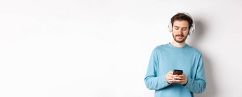 现代年轻的男人。蓝色的运动衫把音乐智能手机听歌曲无线耳机白色背景