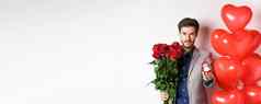 英俊的男人。西装给订婚环花束红色的玫瑰结婚情人节一天站心气球白色背景