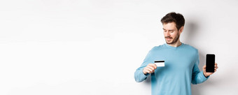 英俊的年轻的男人。胡子显示空智能手机屏幕塑料信贷卡站白色背景