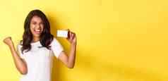 肖像快乐的非裔美国人女模型显示信贷卡大喊大叫快乐快乐购物站黄色的背景