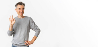 图像英俊的中年男人。灰色毛衣显示标志微笑满意推荐产品批准同意好站白色背景