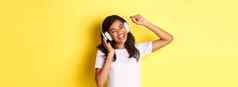 快乐的十几岁的非裔美国人女孩听音乐耳机跳舞乐观的唱歌站黄色的背景