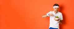 肖像有趣的中年运动员锻炼统一的舔嘴唇吃美味的沙拉体育运动培训站橙色背景