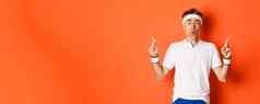 肖像英俊的中年的家伙体育服装指出手指显示促销横幅健身房锻炼站橙色背景