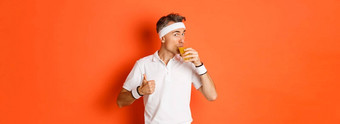 概念锻炼健身房生活方式肖像英俊的中年健身的家伙显示竖起大拇指喝汁站橙色背景