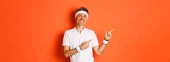 肖像活跃的健康的男人。体育穿运动服微笑指出手指左锻炼促销站橙色背景