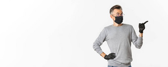 概念冠状病毒生活方式检疫肖像惊讶英俊的中年男人。指出穿黑色的医疗面具手套站白色背景