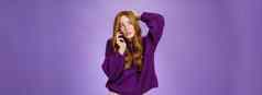 困惑可爱的红色头发的人女使预约移动电话抓回来头眯着眼看思考使选择记住说话智能手机紫色的墙