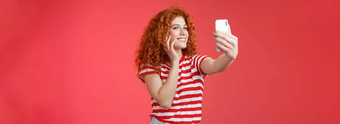 受欢迎的快<strong>乐</strong>的好看的时尚的女博主红色头发的人卷曲的发型感觉漂亮的自我接纳采取自拍提高了手臂持有智能手机摆姿势<strong>愚</strong>蠢的可爱的电话相机红色的背景
