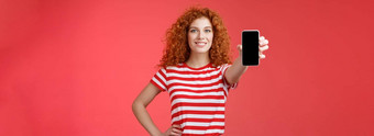 自信好看的红色头发的人卷曲的女人现在很酷的应用程序持有智能手机扩展手显示电话屏幕微笑自信的推荐订阅博客社交媒体
