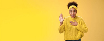 着迷逗乐年轻的迷人的真诚的非裔美国人女孩头巾毛衣新闻手胸部提高棕榈说脏话有前途的站兴奋咧着嘴笑幸福的摆姿势黄色的背景