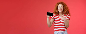 兴奋快乐好看的欧洲红色头发的人卷曲的女孩惊讶显示个人成就分数智能手机游戏显示电话屏幕指出显示讨论太棒了游戏微笑很高兴