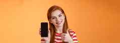 智能手机应用程序保证自信的可爱的友善的红色头发的人女人推荐手机应用程序介绍在线商店网站给翘拇指批准站橙色背景