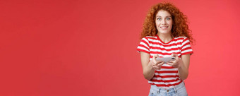 兴奋快乐可爱的红色头发的人卷发女朋友急切的开始学习玩的男朋友游戏逗乐快乐的相机微笑快乐的持有水平智能手机负载应用程序红色的背景