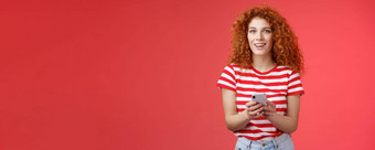 时尚无忧无虑的好看的放松红色头发的人女朋友持有智能手机相机兴奋很高兴转注意朋友回答消息社会媒体写作帖子红色的背景
