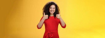 有创意的有魅力的快乐乐观的女人卷曲的头发红色的衣服眨眼批准显示拇指广泛的微笑满意给积极的回复黄色的墙