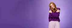 愚蠢的可爱的无忧无虑的红色头发的人女人倾斜肩膀拥抱感觉温暖穿紫色的毛衣微笑广泛的舒适的放松大气紫罗兰色的墙