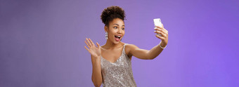 友好的时尚的自信非裔美国人女人银闪闪发光的衣服挥舞着提高了棕榈手势记录视频智能手机问候互联网追随者写博客聚会，派对